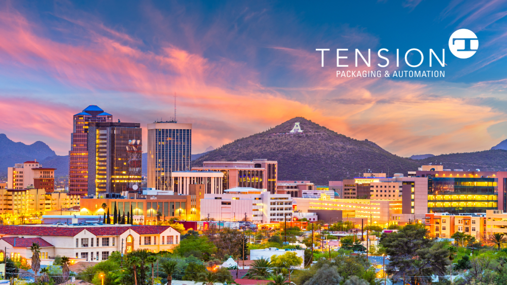 Cityscape of Tucson, Arizona at sunset, with colorful clouds, downtown buildings, and a mountain with a large white A on a mountain in the background. Tension Packaging & Automation logo appears in the upper right corner.