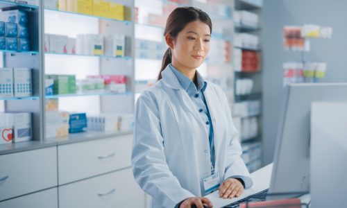 Pharmacy Drugstore: Beautiful Asian Pharmacist Uses Checkout Counter Computer, Does Inventory Checkup, Online Prescription of Medicine Packages, Drugs, Vitamin Boxes, Supplements, Health Care Products